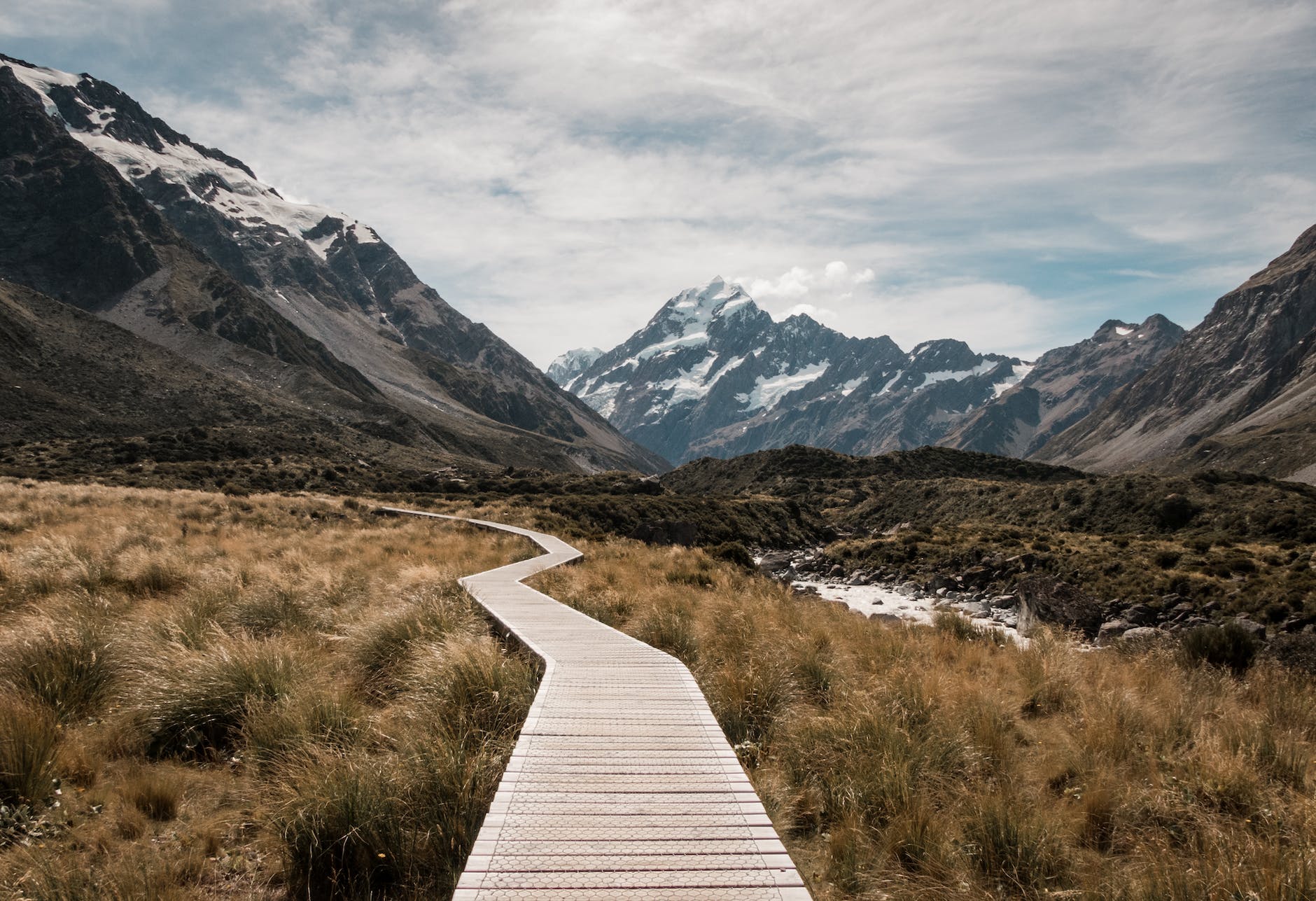 brown wooden dock surrounded with green grass near mountain under white clouds and blue sky at daytime